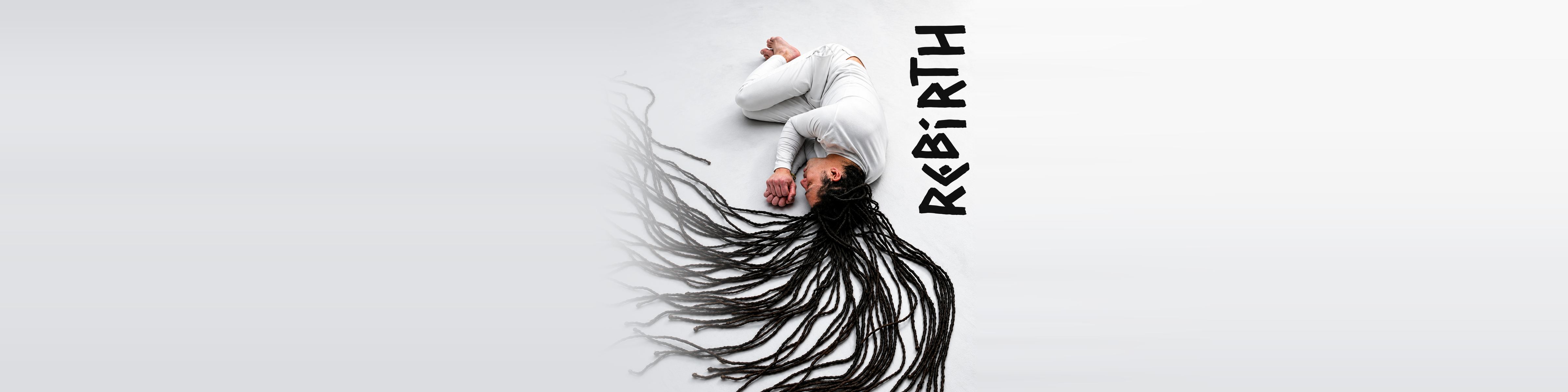 Kevin Alva lying on a white floor with his long dreadlocks spread out, next to the word Rebirth
